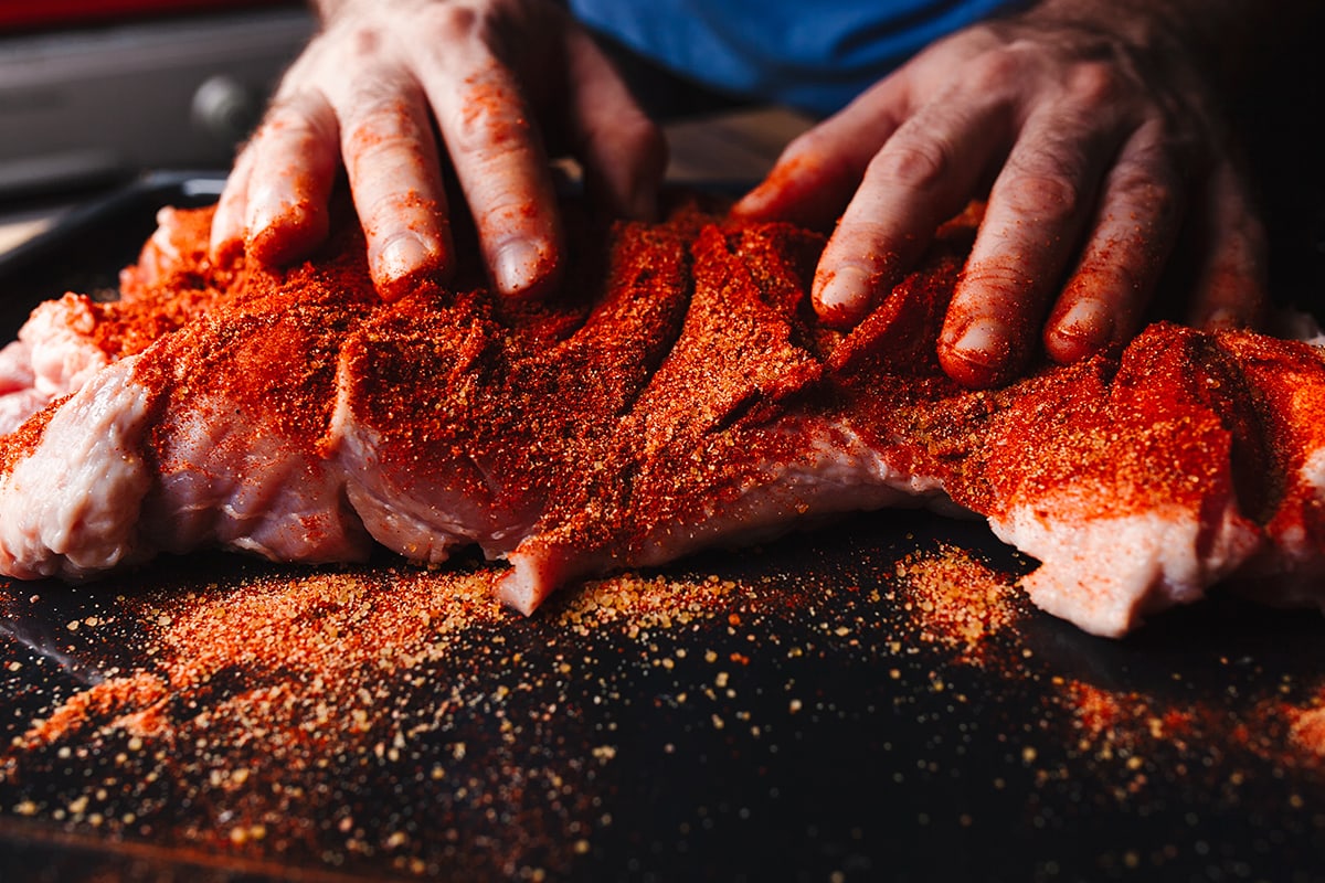 Man preparing raw piece of meat, rubbing different spices and herbs in it before roasting