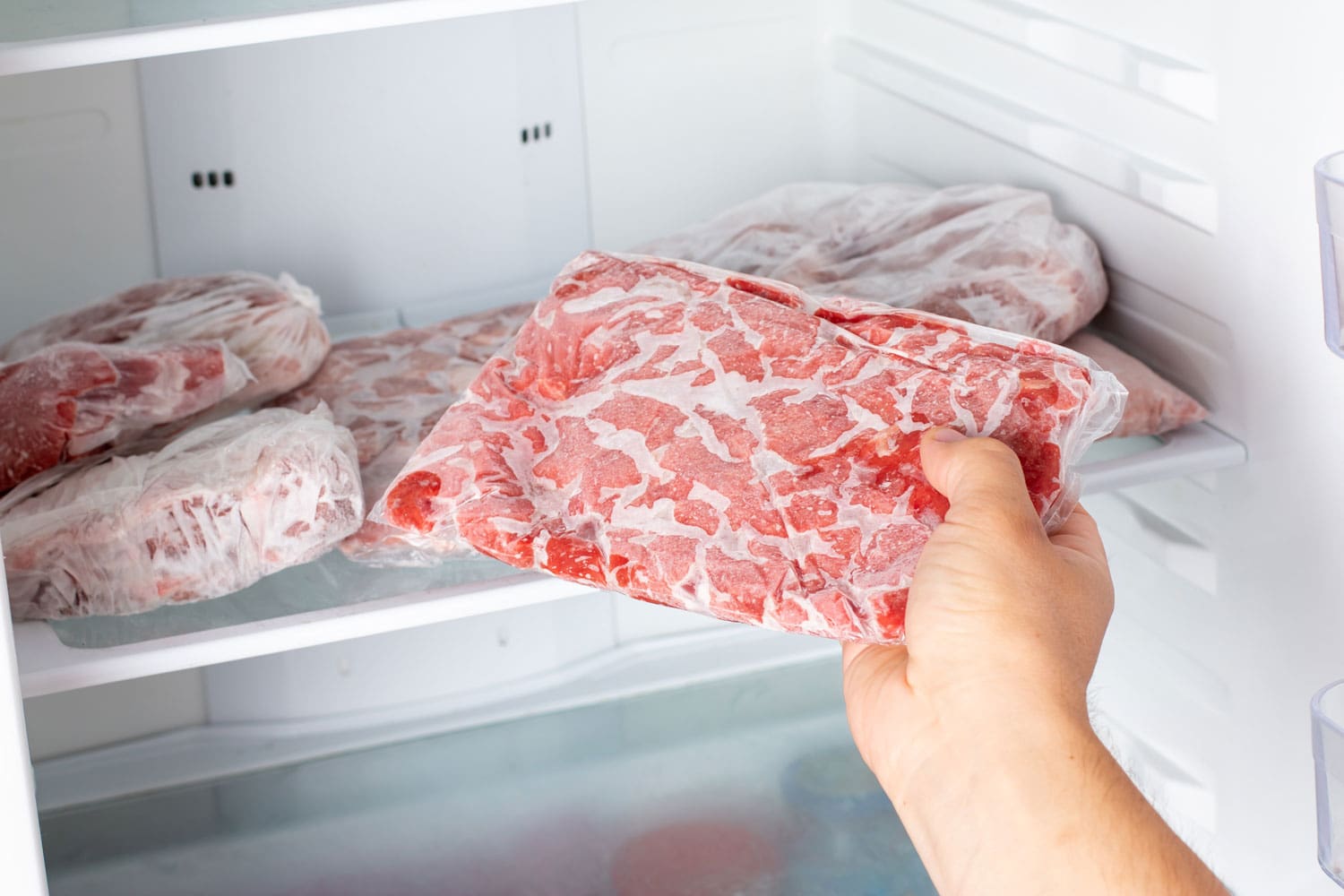 The Man takes out a bag of frozen meat from the freezer in the kitchen at home. Frozen food