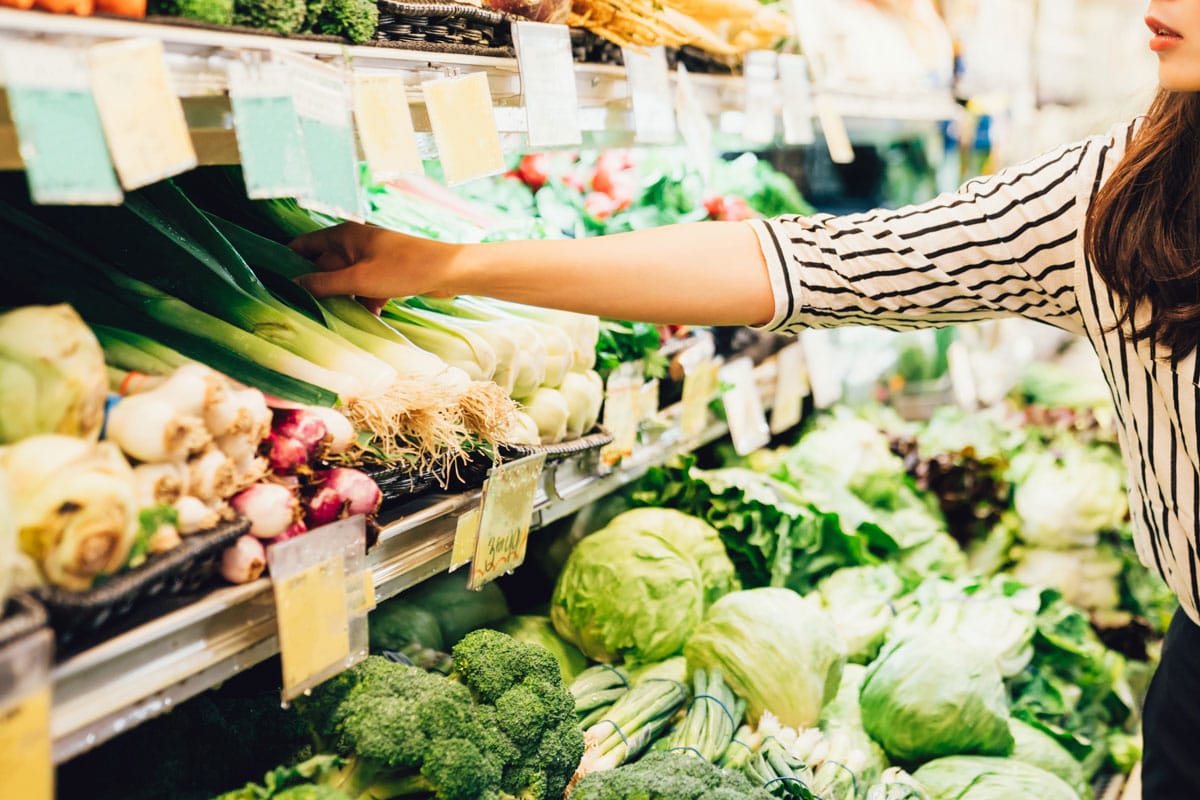 年轻的中国女士拿着绿叶蔬菜，在冷开的冰箱上挑选青葱