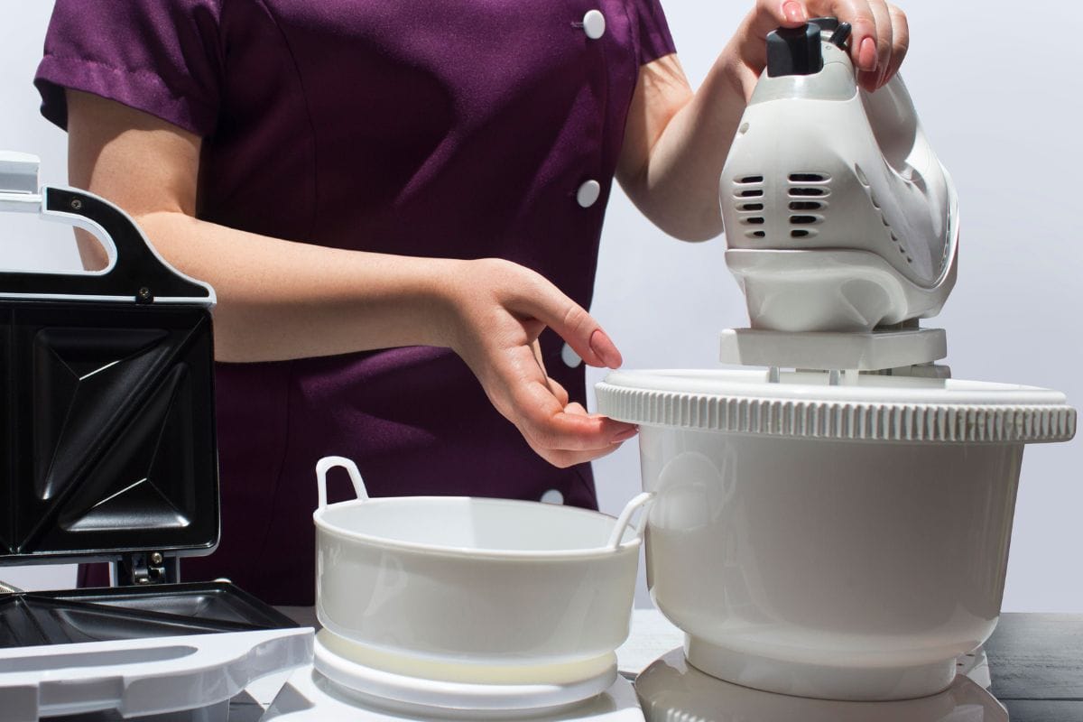 一个年轻woman-cook准备做饭,站在桌子和厨房电器:烤面包机、称重机和食品搅拌机。雷电竞官网网址