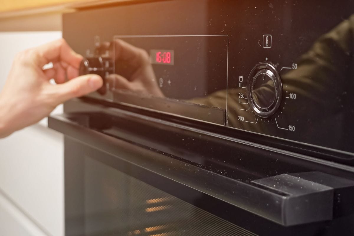 人调整温度和设置操作模式在现代厨房的烤箱。雷电竞官网网址管家准备晚餐使用在家烹饪用具,阳光。